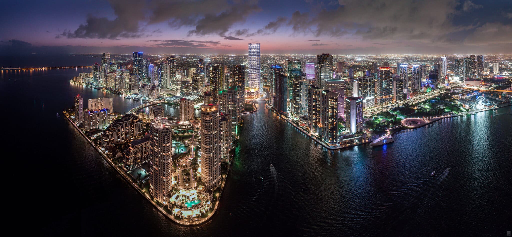 Aerial night view of Brickell and Downtown Miami skyline with waterfront high-rises and city lights.