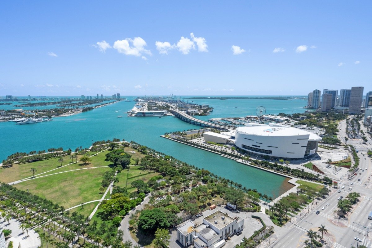 Aerial view of Biscayne Bay, Maurice A. Ferré Park, and Kaseya Center in Downtown Miami under clear blue skies.