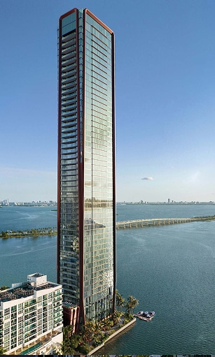 A sleek, modern skyscraper with glass exteriors stands by a large body of water. The clear blue sky enhances the building's towering presence.