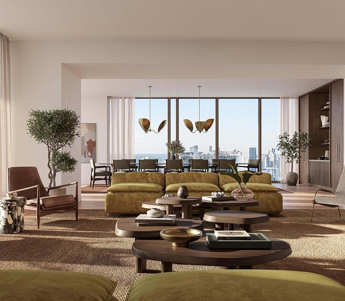 Spacious modern living room with green sofas, wooden tables, and large windows overlooking a cityscape. Warm tones create a cozy, inviting atmosphere.