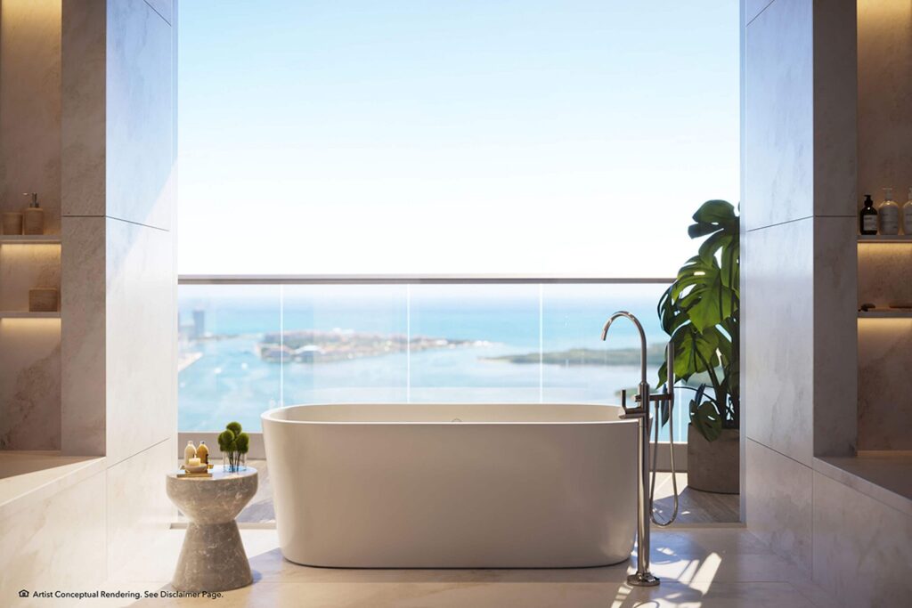 Luxurious bathroom with a freestanding tub facing a large window showcasing an ocean view. Marble walls, a plant, and candles create a serene atmosphere.