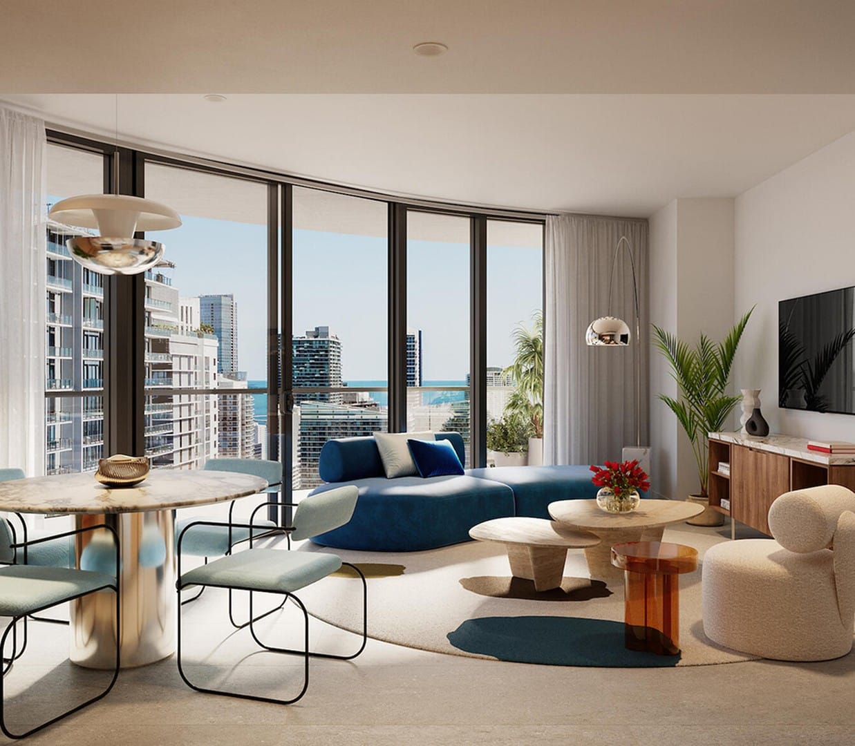 Modern living room with large windows offering a city and ocean view. Features a blue couch, round coffee tables, dining area, and decorative plants. Bright and spacious ambiance.