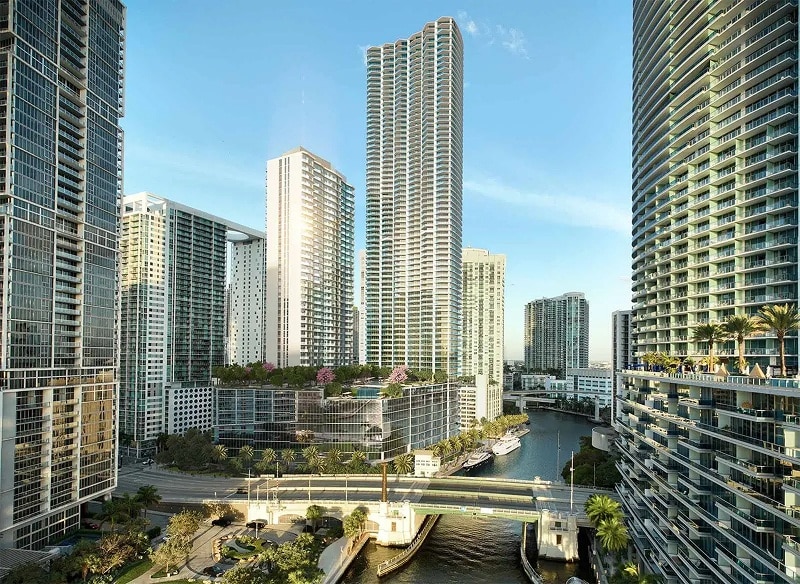 Cityscape view featuring tall, modern skyscrapers in a vibrant urban area with a waterway and bridges below, under a clear blue sky.