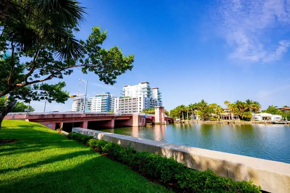 Waterfront view of Allison Island with bridge access, calm bay waters, palm-lined lawns, and modern condominium buildings in Miami Beach.