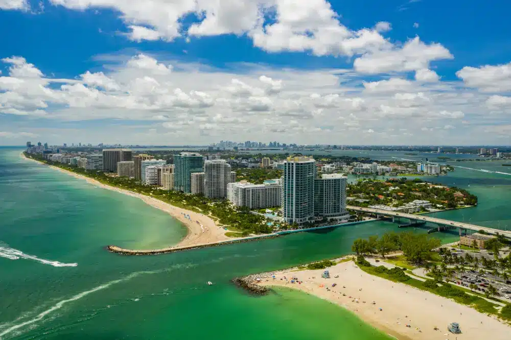 Aerial view of Bal Harbour with oceanfront condominiums, sandy beaches, Haulover Inlet, turquoise waters, and Miami Beach skyline beyond.