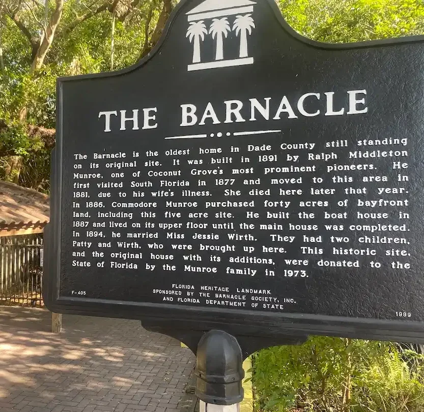 Historic marker sign for The Barnacle at Coconut Grove park surrounded by trees and brick walkway in Miami