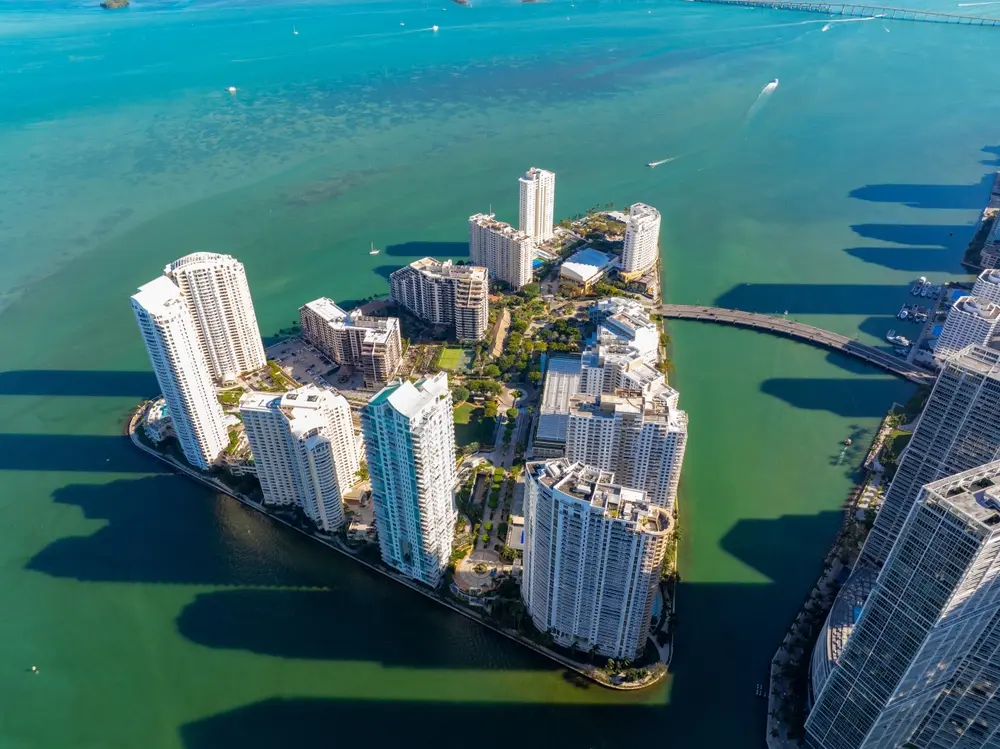 Aerial view of Brickell Key with luxury condominium towers surrounded by Biscayne Bay, connected to Brickell by bridge access.