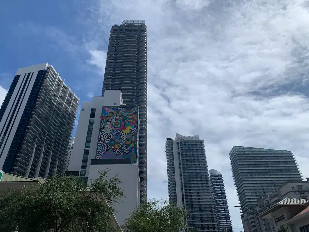 Brickell Miami skyline with modern high-rise condo towers and a colorful mural façade under a partly cloudy South Florida sky.