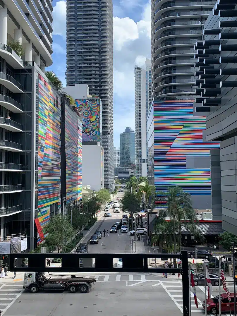 Brickell Miami street view framed by modern high-rise condos with colorful mural façades, palm trees, and urban traffic below.