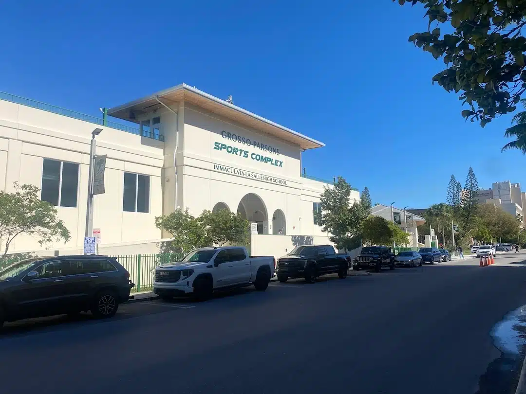 Front view of Grosso Parsons Sports Complex and campus building at La Salle High School in Miami with street and parked cars