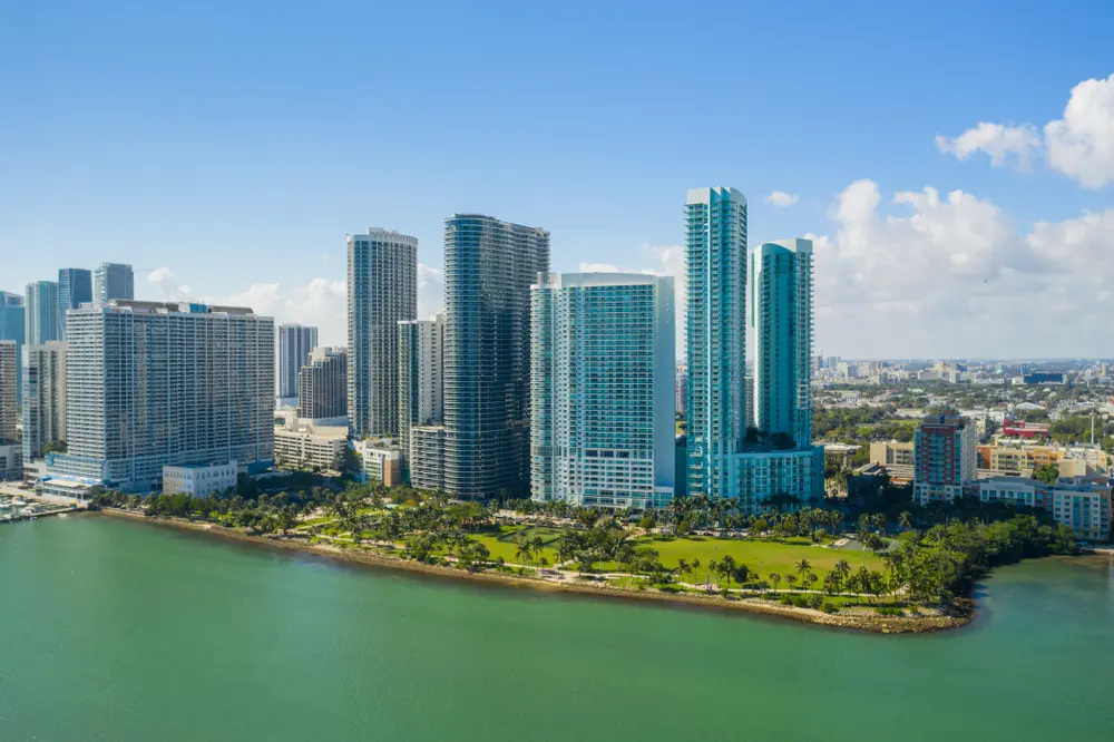 Aerial view of Edgewater Miami skyline with modern high-rise condos along Biscayne Bay, palm-lined parks, and downtown Miami in the distance.