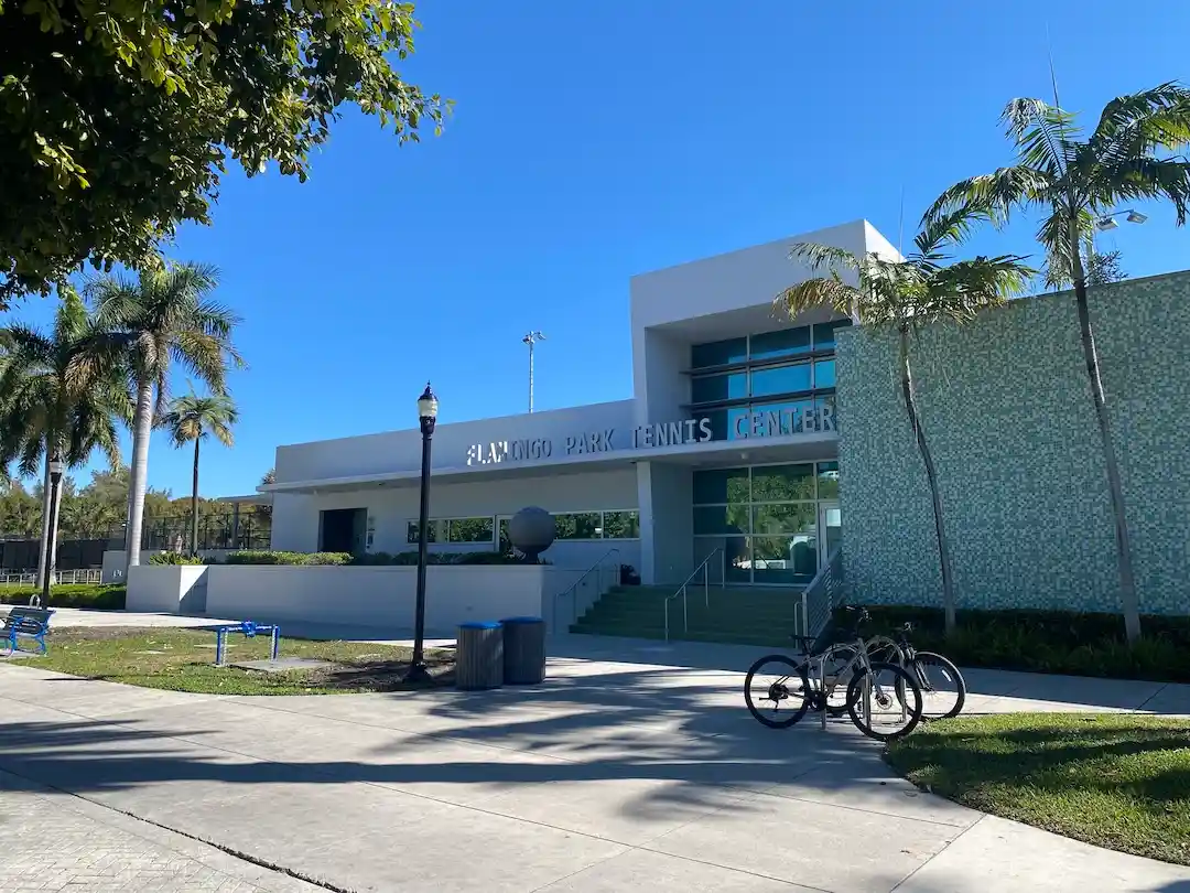 Exterior view of the Flamingo Park Tennis Center with palm trees and pedestrian walkway in Miami Beach.