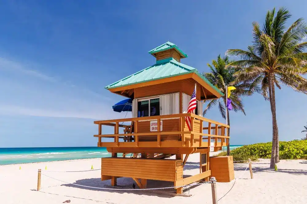 Lifeguard tower on Key Biscayne beach with palm trees, white sand, turquoise ocean, and clear skies typical of South Florida.