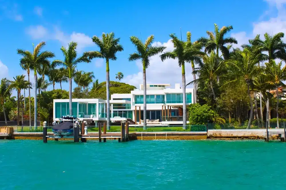 Modern waterfront home in Key Biscayne with private dock, palm trees, turquoise bay waters, and contemporary coastal architecture.
