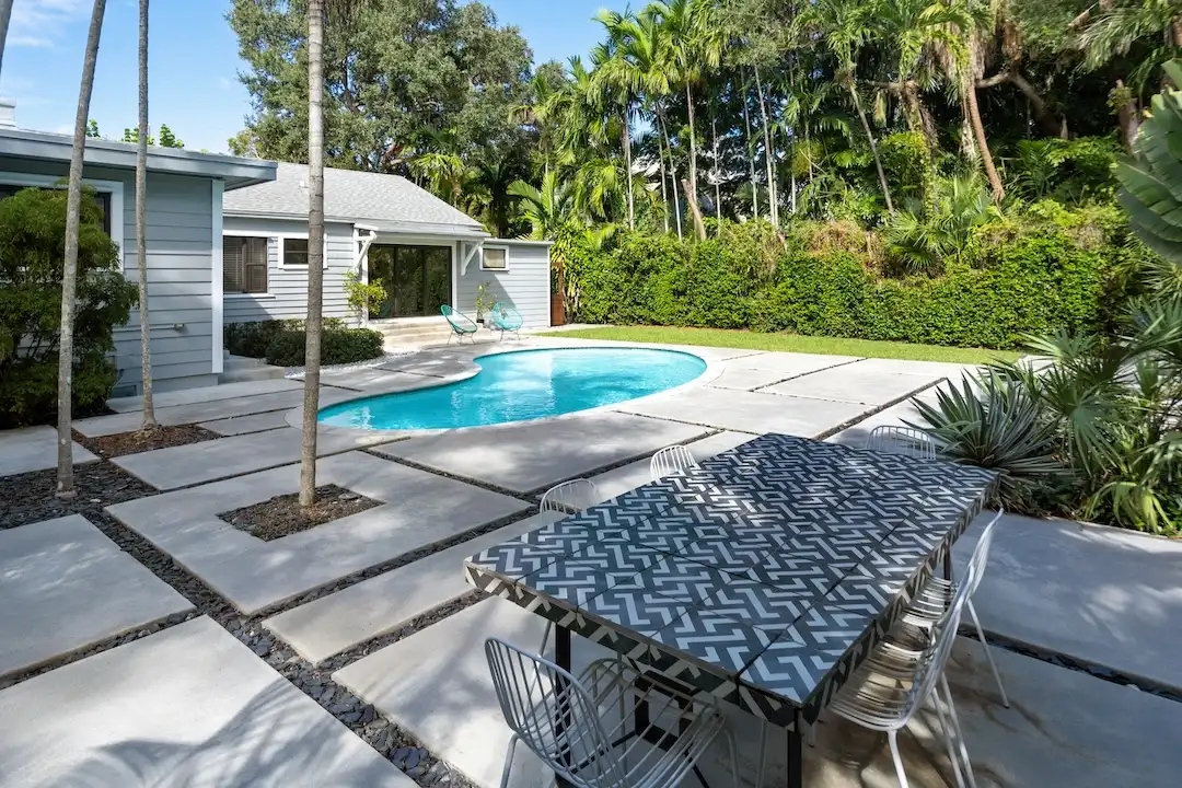 Backyard pool and patio area with outdoor dining space and tropical landscaping in Miami.