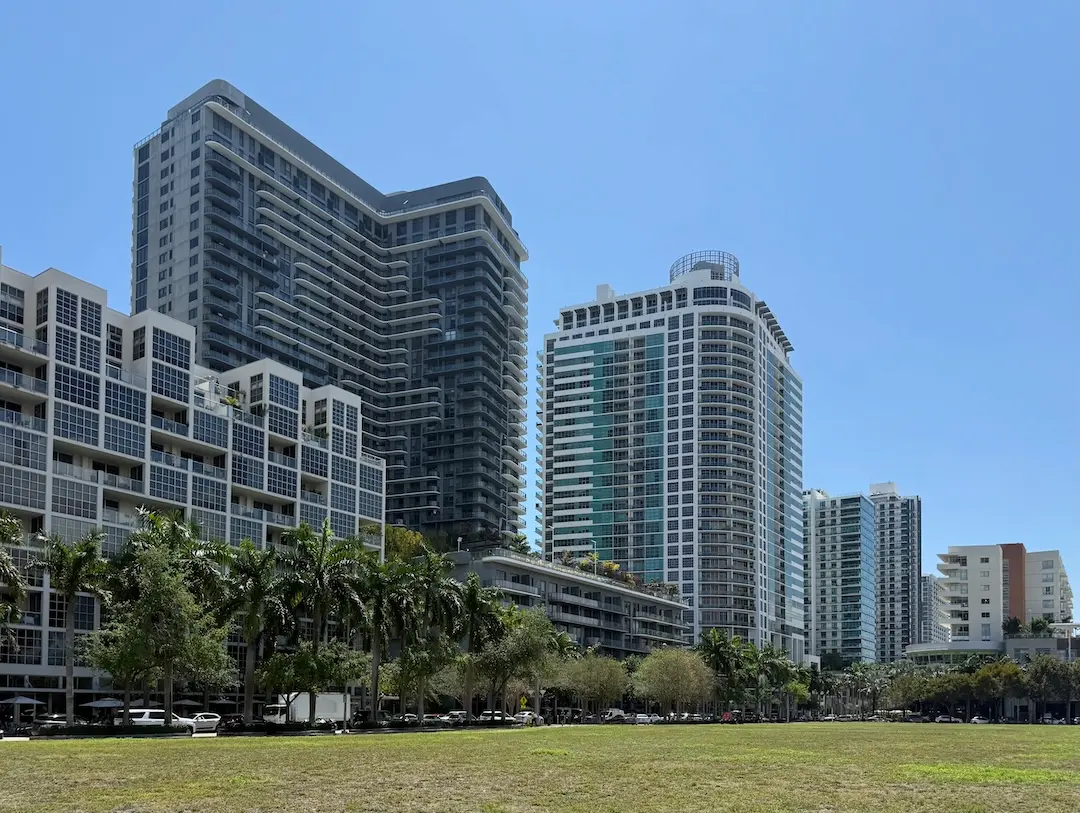 Midtown Miami skyline featuring modern condominium towers, palm-lined streets, and open green space under a clear South Florida sky.