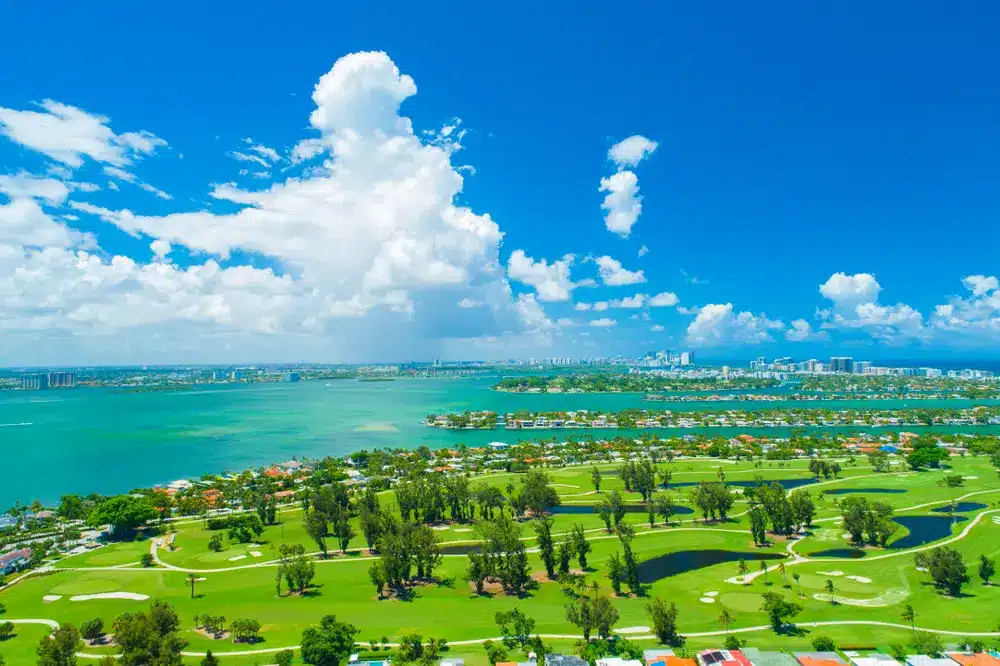 Aerial view of Normandy Isle golf course in Miami Beach with green fairways, water features, Biscayne Bay, and the city skyline in the distance.