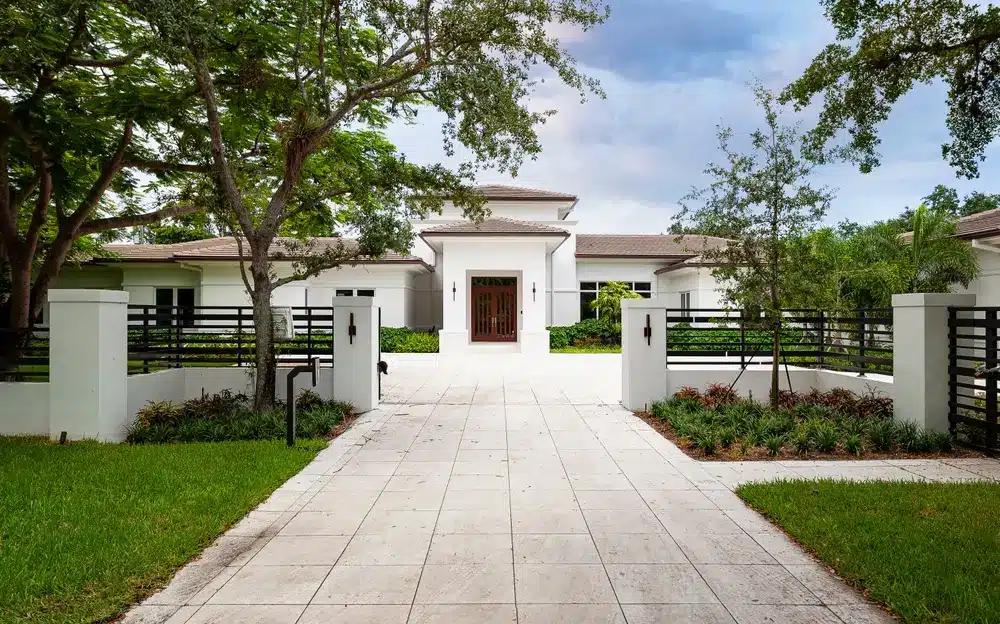 Luxury single-family home in Pinecrest with gated driveway, manicured landscaping, mature trees, and elegant contemporary design.