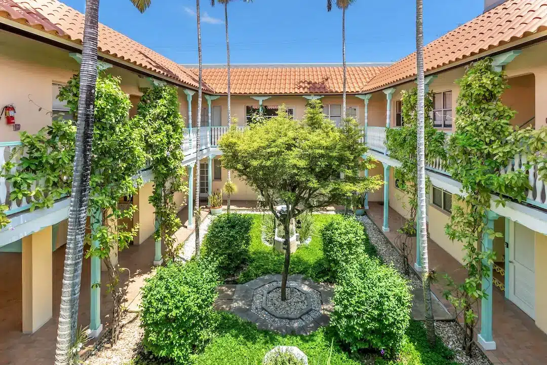 Historic South Beach Miami courtyard condominium featuring a lush landscaped garden, Spanish-style architecture, palm trees, and interior walkways.