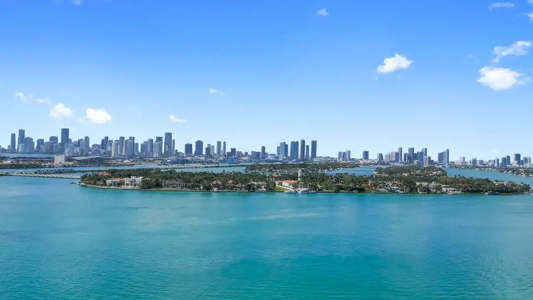 Aerial view of Star Island in Miami Beach with luxury waterfront homes, turquoise Biscayne Bay, and the Downtown Miami skyline in the background.