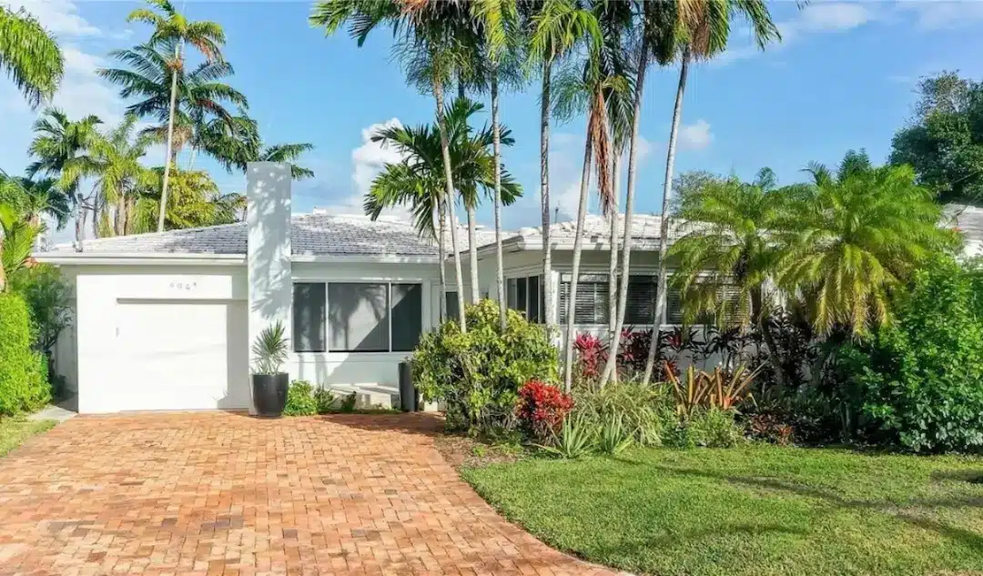 Single-family home in Surfside, Miami with a brick driveway, tropical landscaping, and palm trees in a quiet residential setting.
