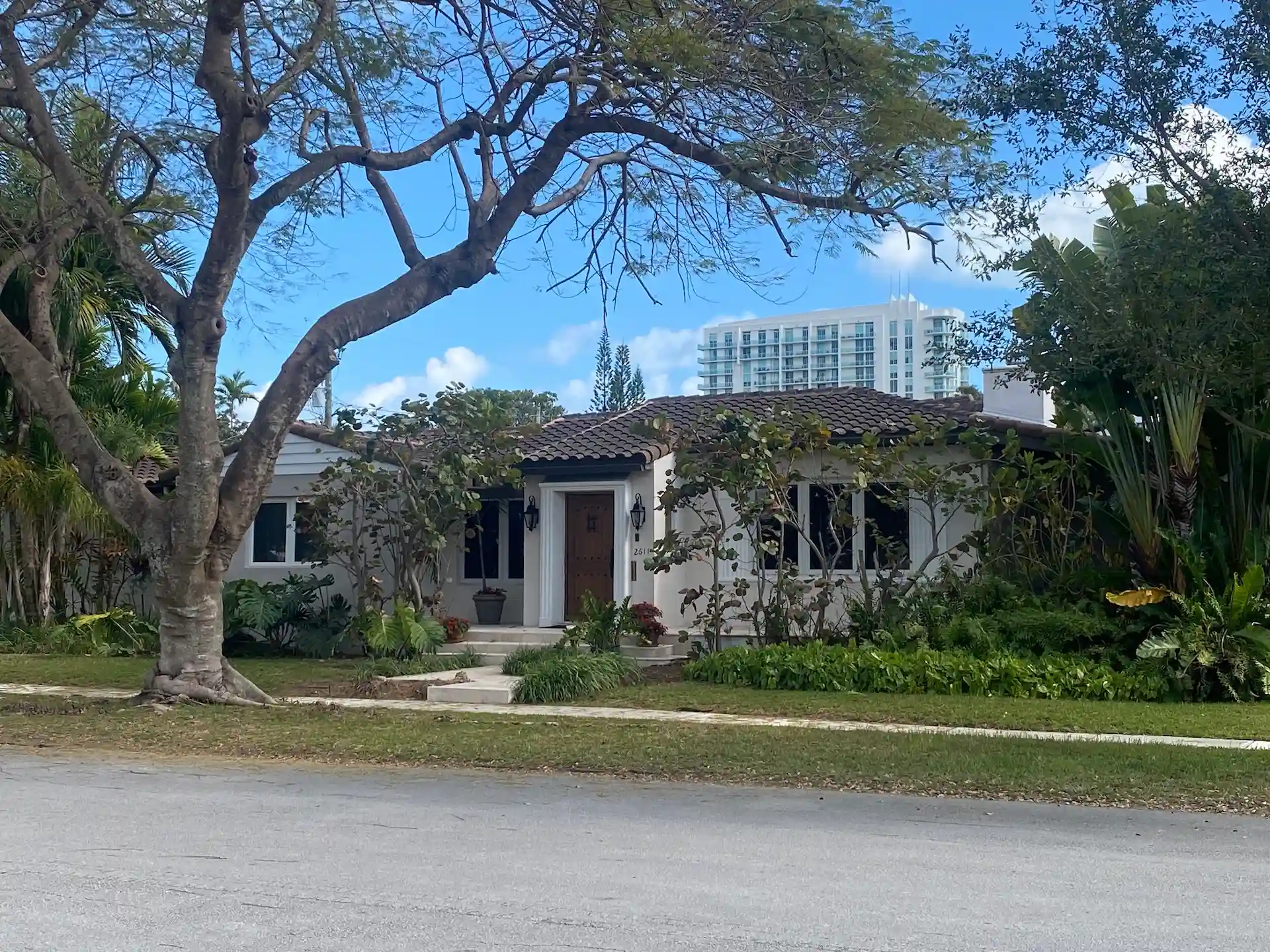 Spanish-style single-family home on a tree-lined residential street in The Roads Miami with lush landscaping and tropical greenery.